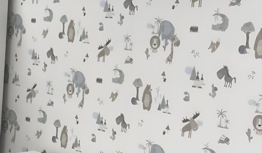 Pared empapelada con motivos infantiles en tonos neutros y mobiliario blanco.